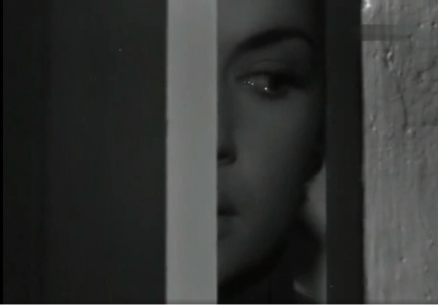 Una persona observa con expresión seria a través de una rendija en una puerta en una escena en blanco y negro.

Description generated by AI