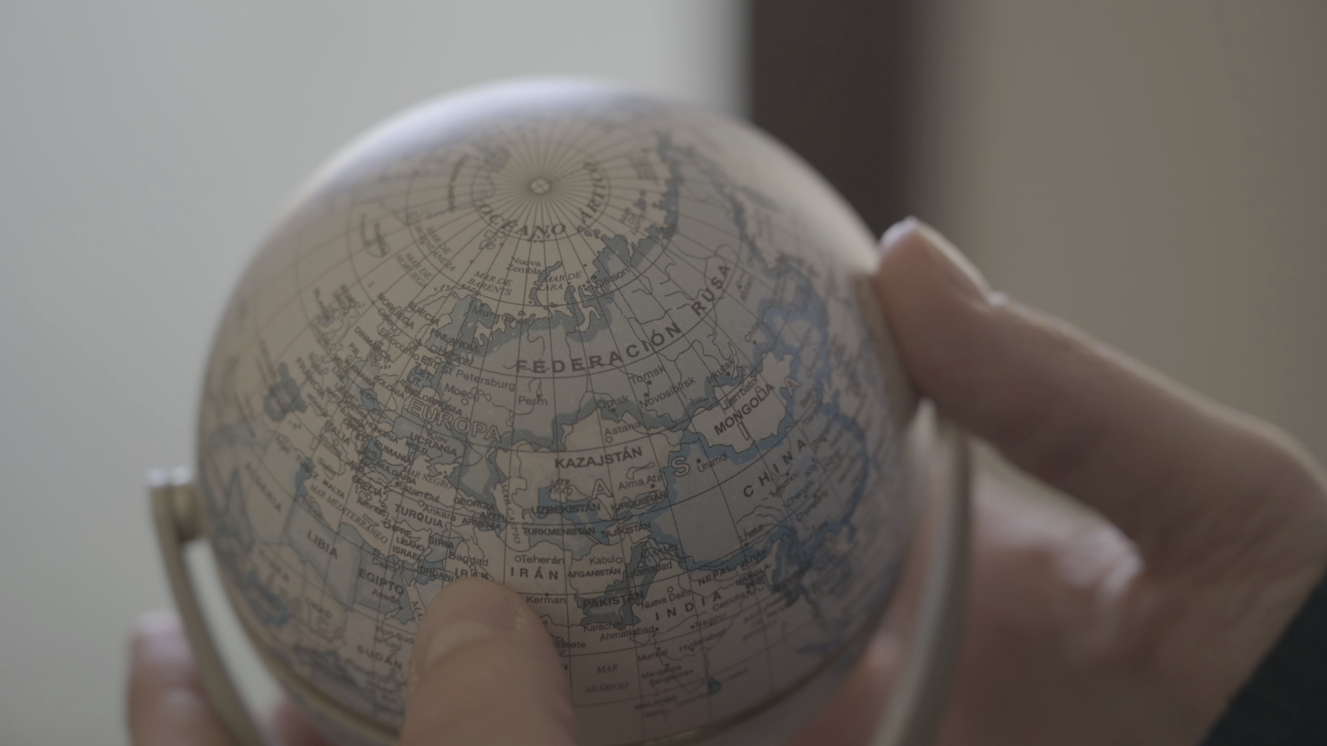 Una persona sostiene y señala un pequeño globo terráqueo que muestra principalmente la región de Europa y Asia.

Description generated by AI