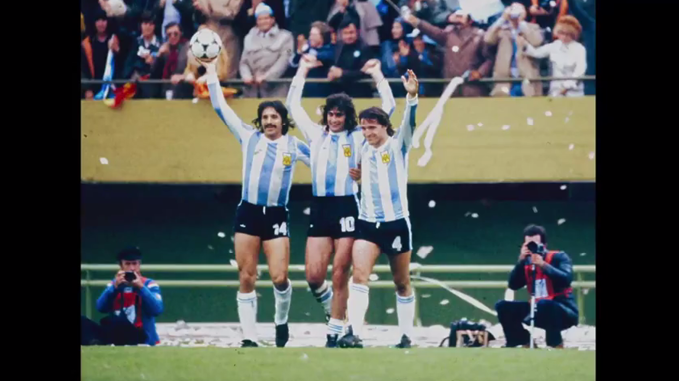 Tres adultos con uniformes de fútbol celeste y blanco celebran en un estadio mientras sostienen un balón y levantan los brazos frente a una multitud.

Description generated by AI